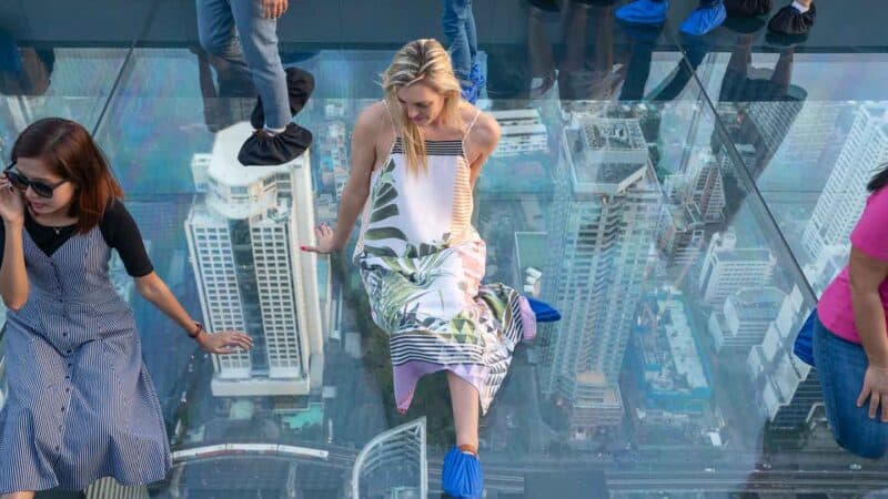 Woman sitting on the glass floor on the Mahanakhon Skywalk - Tallest building in Bangkok