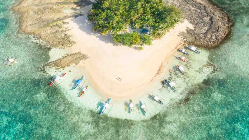 Drone Photo of Guyam Island - Philippines boats parked in aqua water white san on small island 
