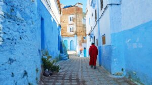 Man in a red robe walking in the town of Chefchaouen Morocco - Top Places to Visit