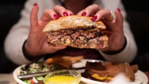 An APV II Burger cut in half held in two hands by a woman - Best Milwaukee Burger