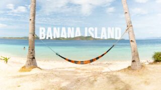 Hammock on the beach of Banana Island stretched between two palm trees with white text for featured image