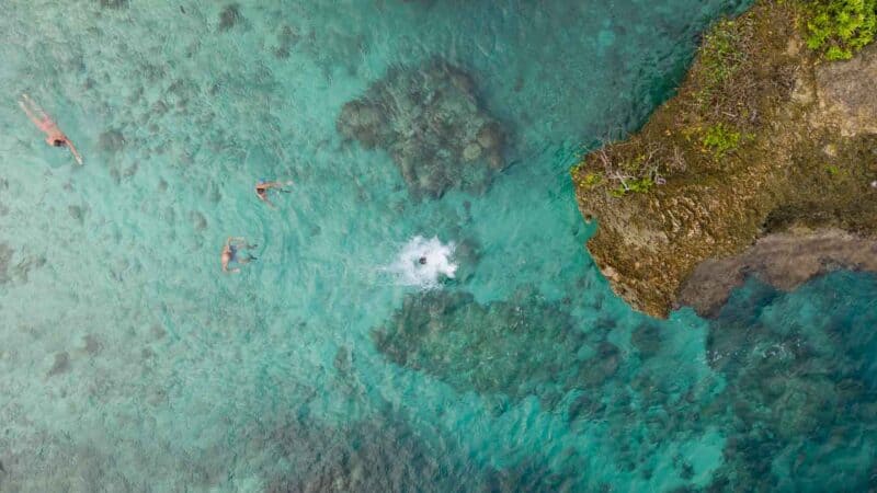 Photo of a person cliff jumping at Magpupungko Rock Pools splashing into clear aqua colored water