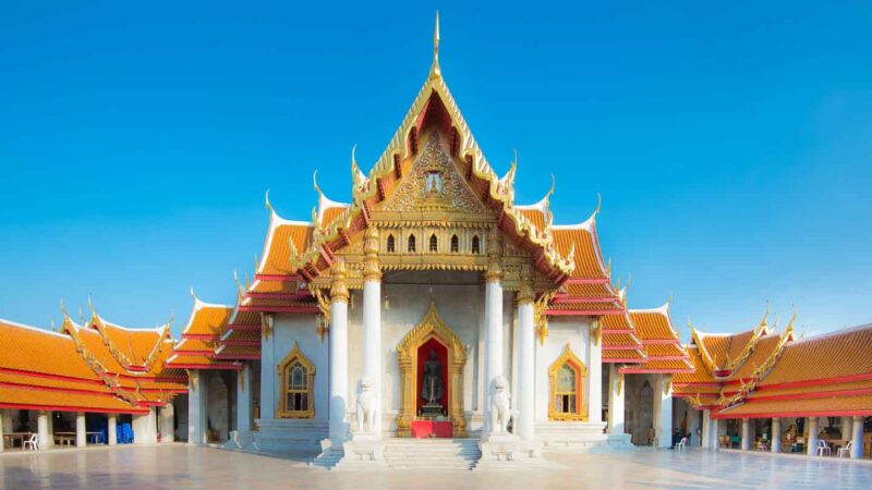 Large white tempe with organe and green roof with many gold accents in a traditional Thai style - Wat Benchamabophit temple in the Thai capital of Bangkok