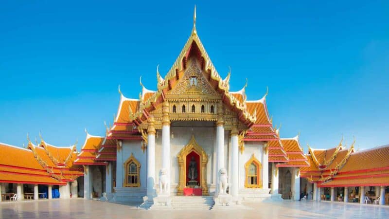 Large white tempe with organe and green roof with many gold accents in a traditional Thai style - Wat Benchamabophit temple in the Thai capital of Bangkok