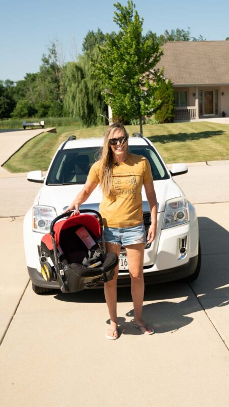 woman holding the Doona car seat stroller travel sysem in front of a car in a driveway