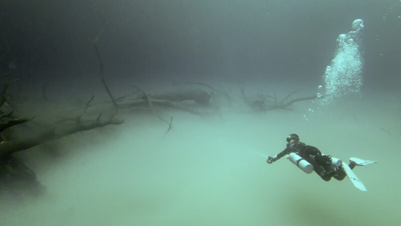 single diver with tech equipment and side mount tanks heads toward the talus cone and hydrogen sulfide cloud of cenote angelita