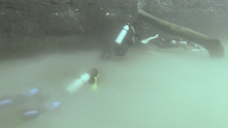 3 divers swimming in the halocline of cenote angelita with the image slightly blurred due to the mixing of fresh and salt water