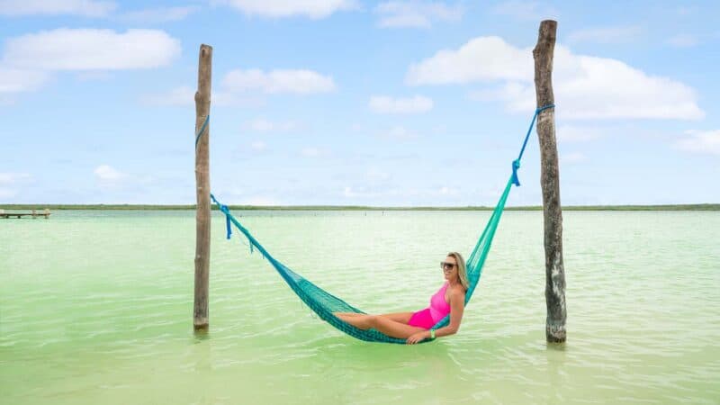 Woman in the hammocks of Kaan Luum hanging over greenish blue water