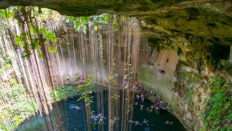 View looking down in to Il Kil Cenote swimmers and cliff jumpers inside of a lush cenote