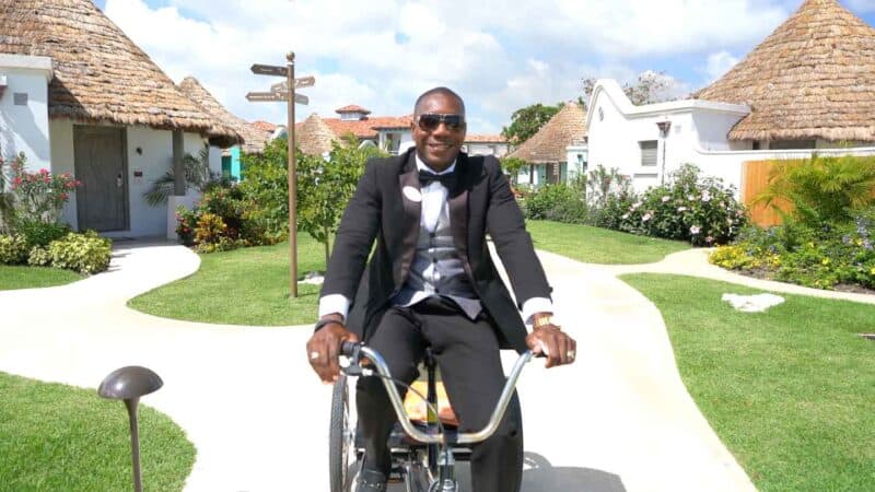 A butler dressed in black riding a bike at Sandals Resorts Barbados location