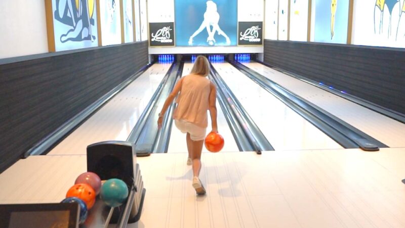 woman bowling with and orange ball at Sandals Royal Barbados Private bowling lanes
