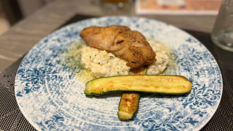 Grouper served on a bed of rizzotto with zucchini on a blue plate at Society Table Restaurant in St. Pete Beach FL 