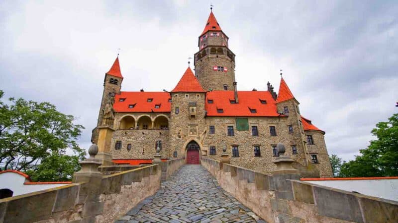 exterior view of Bouzov Castle with a orange red roof and light brown stone facade