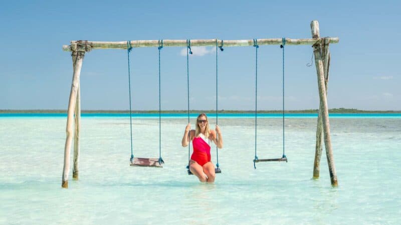 woman in a red swimsuit sitting on a water swing at Cenote Cocalitos in Bacalar