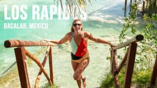 woman standing at the entrance of Los Rapidos in Bacalar Mexico holding a wooden rail with clear blue water behind