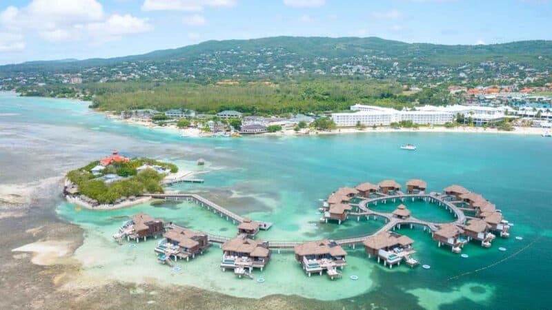 Drone photo of Sandals Royal Caribbean see from above the overwater bungalows looking back toward the main resort