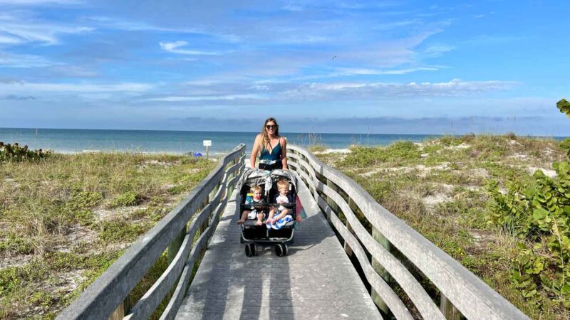 Mom on a beach boardwalk with double stroller Zoe Twin with two kids in Florida