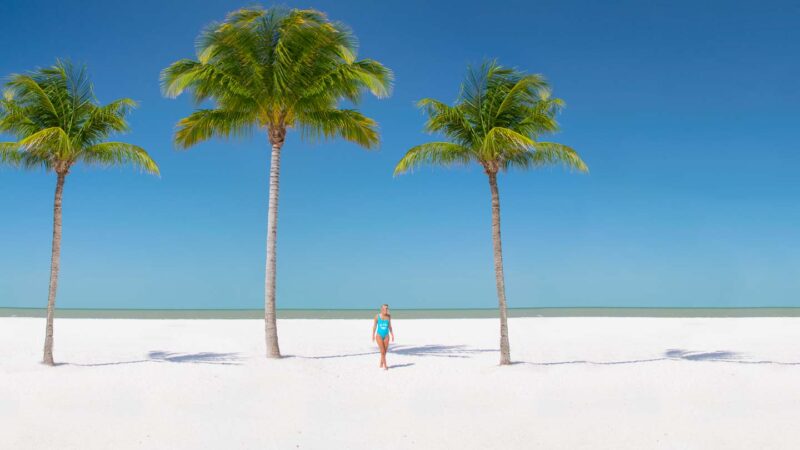 Fort Myers Beach white sand beach with palm trees and women in blue swimsuit