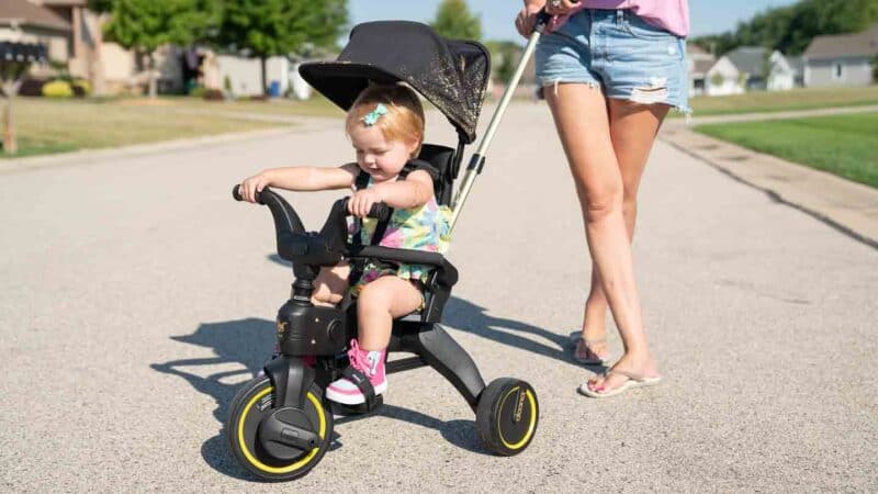 Doona liki trike with toddler riding and mom standing behind it