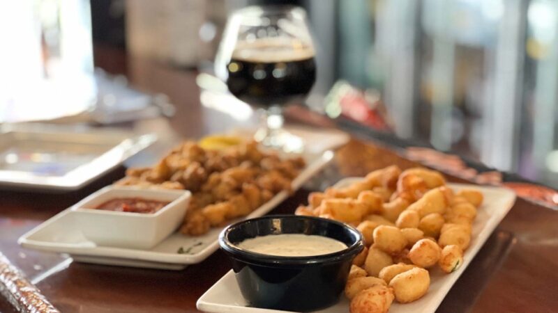 cheese curds on a plate on a bar with a beer in the background 
