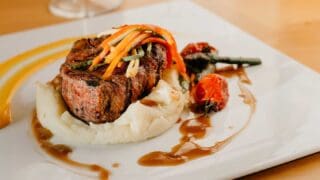 steak and mashed potatoes on a plate with a sauce and garnish at a restaurant