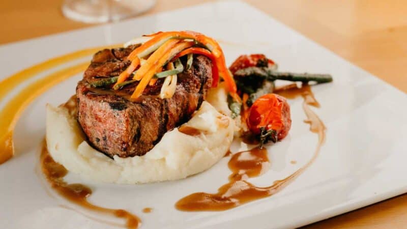 steak and mashed potatoes on a plate  with a sauce and garnish at a restaurant