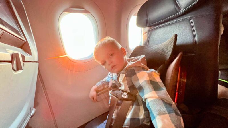child sitting in a toddler airplane car seat on the airplane