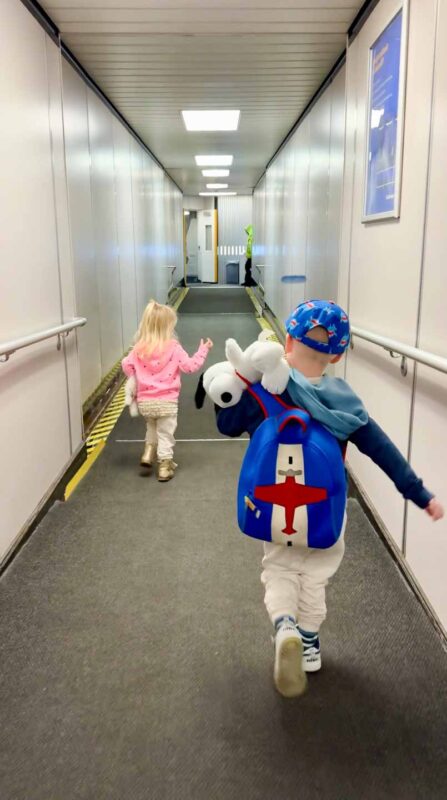 family flying with kids walking on the jet bridge to the airplane