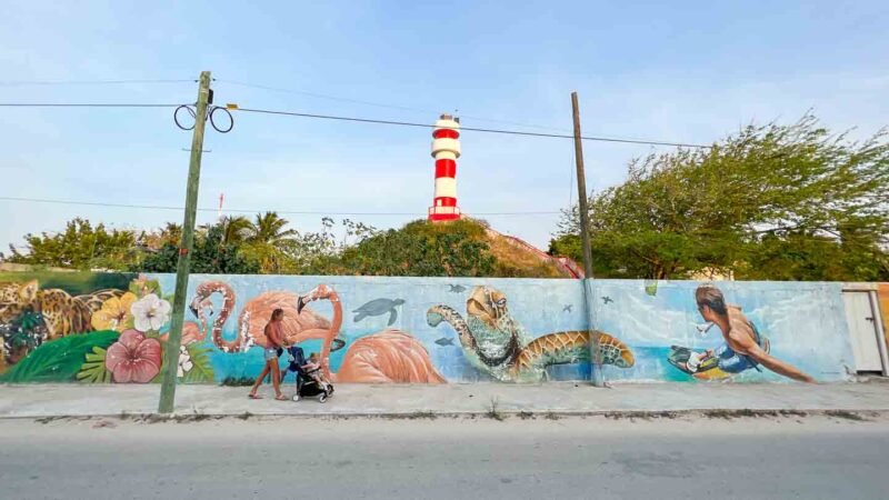 Woman with stroller walks past colorful street art in El Cuyo Mexico