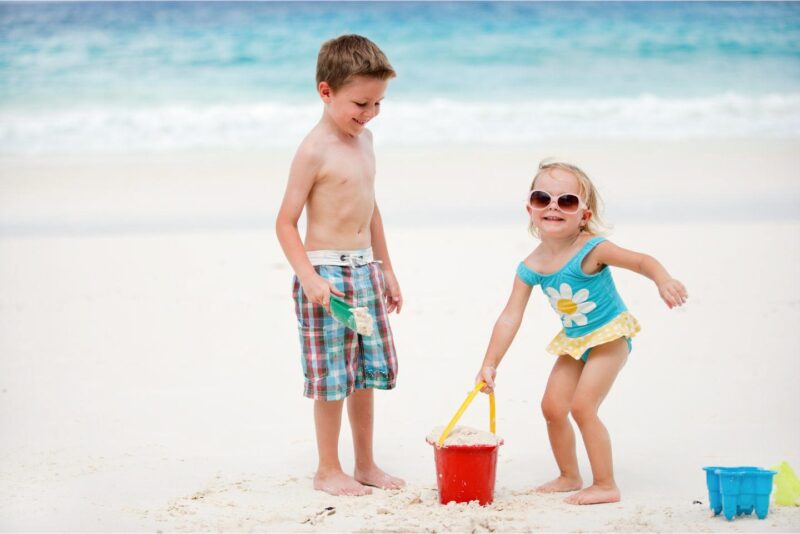 boy and girl toddler playing on the beach with beach buckets