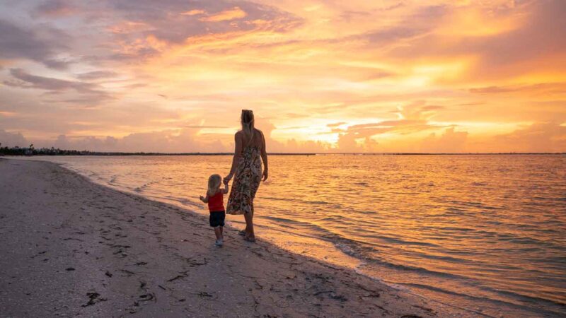 Woman and daughter walking on the beach at sunset in Sanibel Island