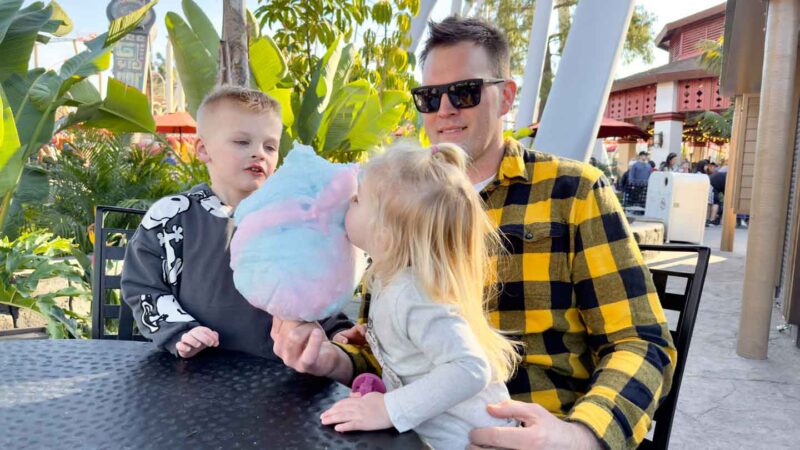 Father and kids eating cottong candy at a theme park