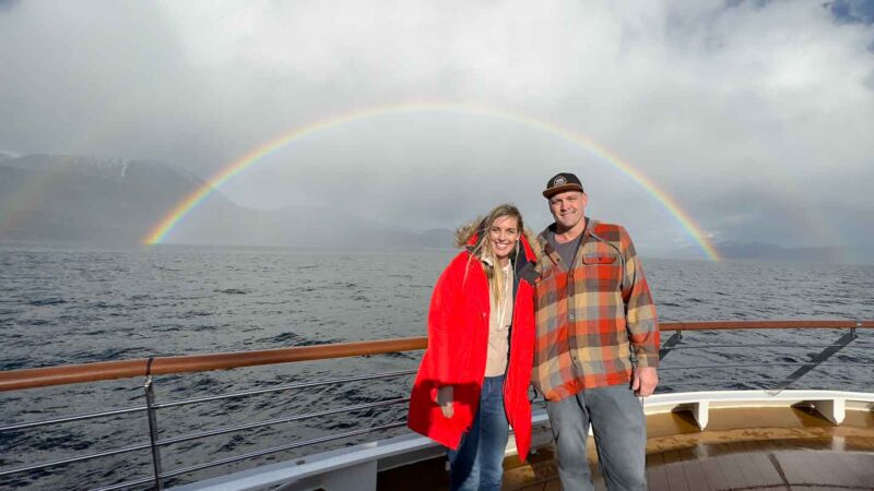 Rainbow in Antarctica with a couple on the deck of Atlas Ocean Voyages cruise ship