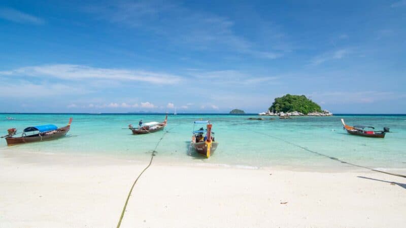 Thai boats in the water on Sunrise Beach Koh Lipe on a sunny day