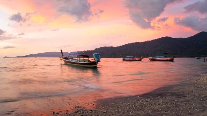 Thai boats in the water on Sunset Beach in Koh Lipe Thailand